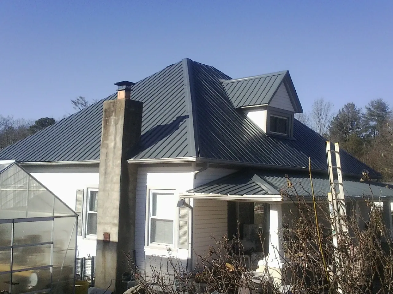 Dark blue standing seam metal roof on a white farmhouse with dormer — Slate & Tile Roof Repair by Roofing Brothers in Dillard