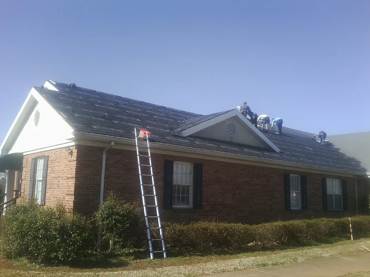 Crew tearing shingles off a brick ranch roof with a ladder set — Metal Roof Repair work by our crew in Dillard