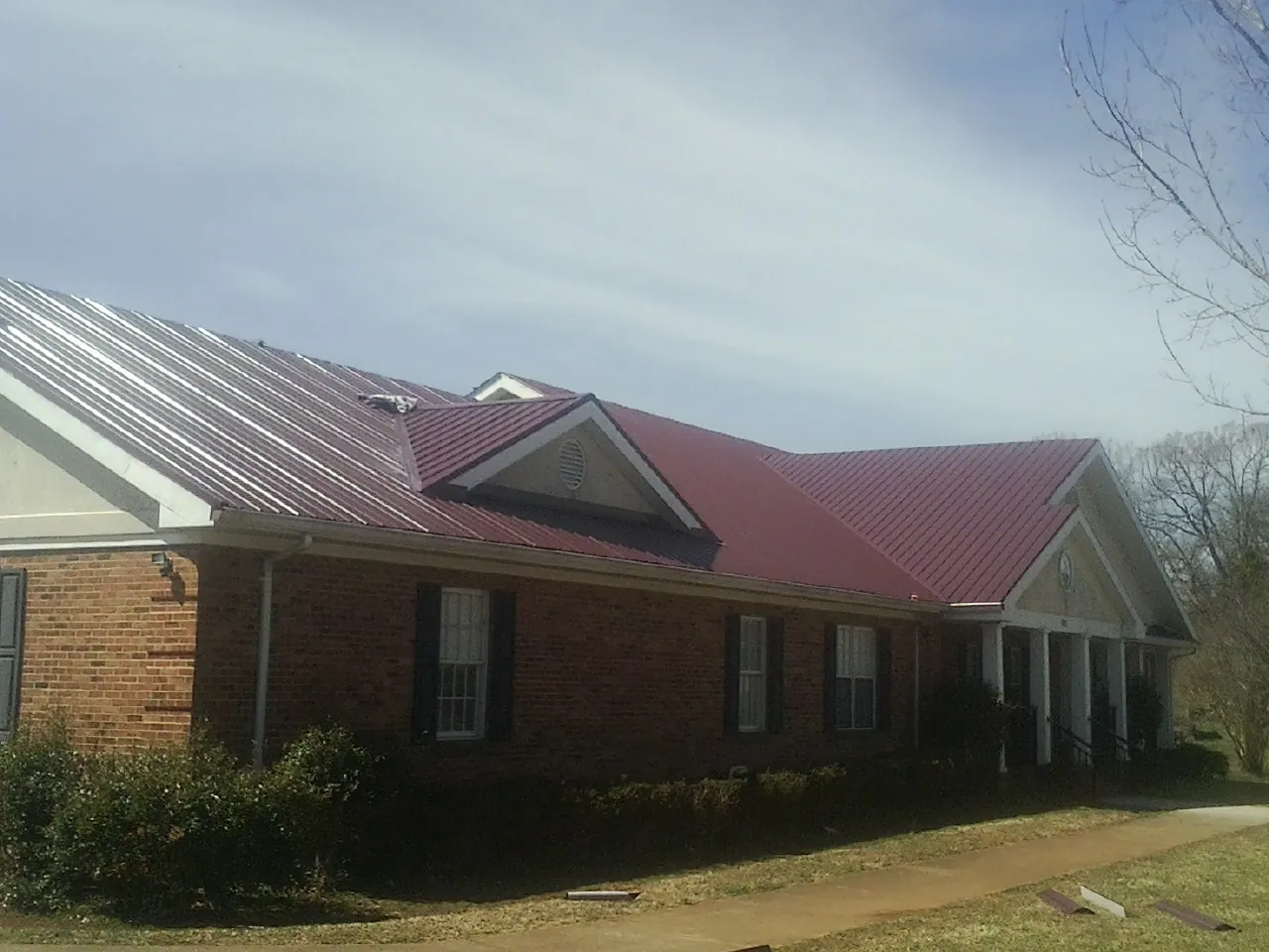 Red metal roof with gabled entries on a long brick building, from a Hail Damage Roof Repair job in Dillard
