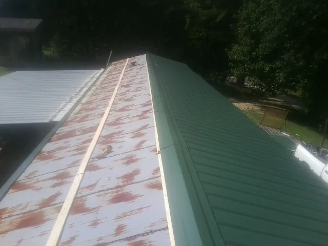 Old rusted panels beside newly installed green metal roofing — Wind Damage Roof Repair by Roofing Brothers in Dillard