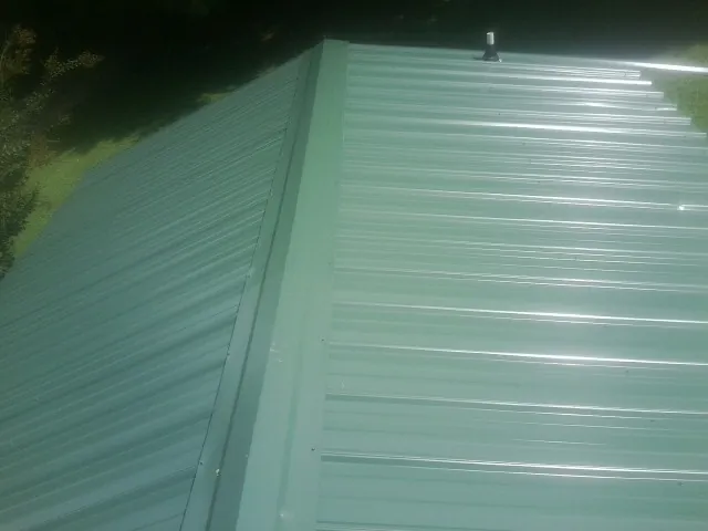 New green metal panels meeting at the ridge of a roof — Flat Roof Repair work by our crew in Dillard