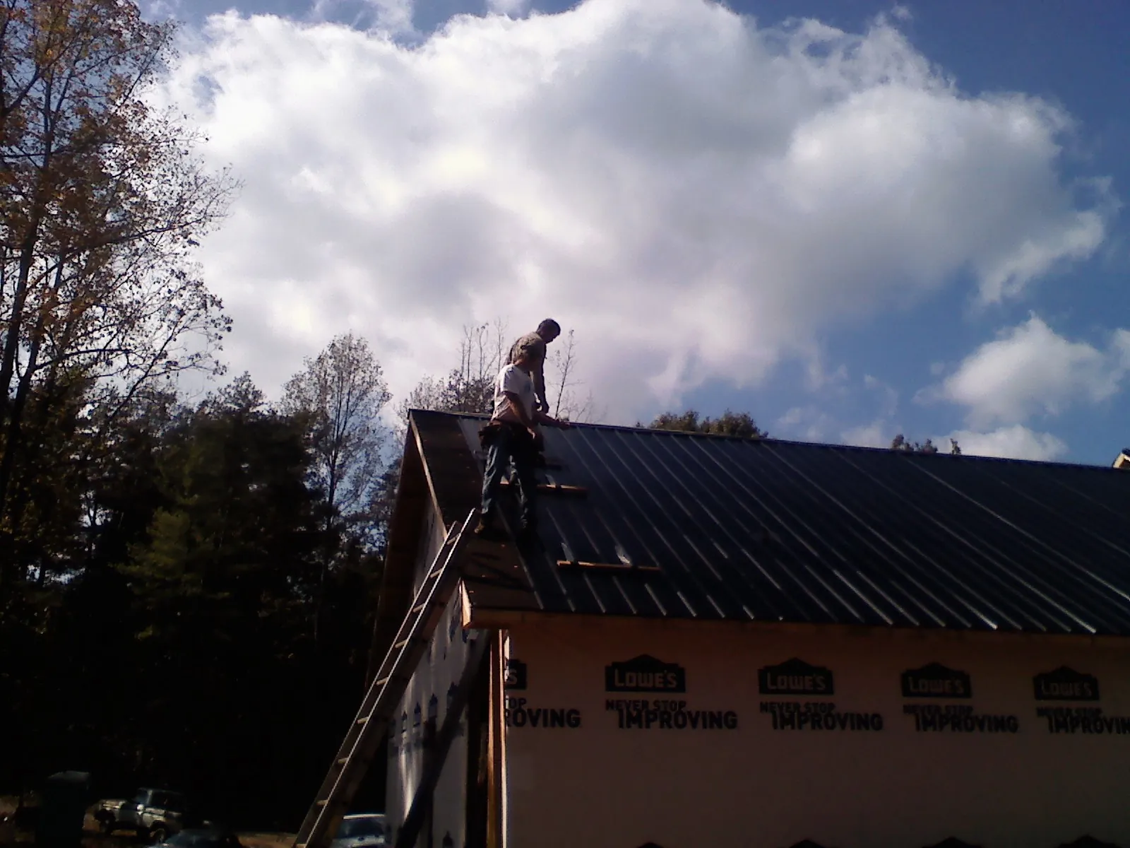 Roofer fastening dark metal panels high against a cloudy sky, from a Roof Inspection job in Dillard